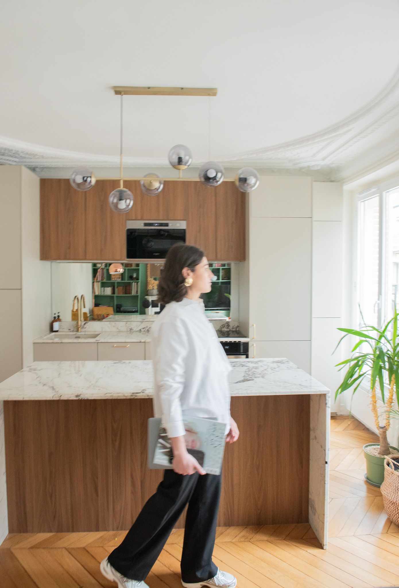 Woman in white sweater walking through modern kitchen with globe pendant brass chandelier.