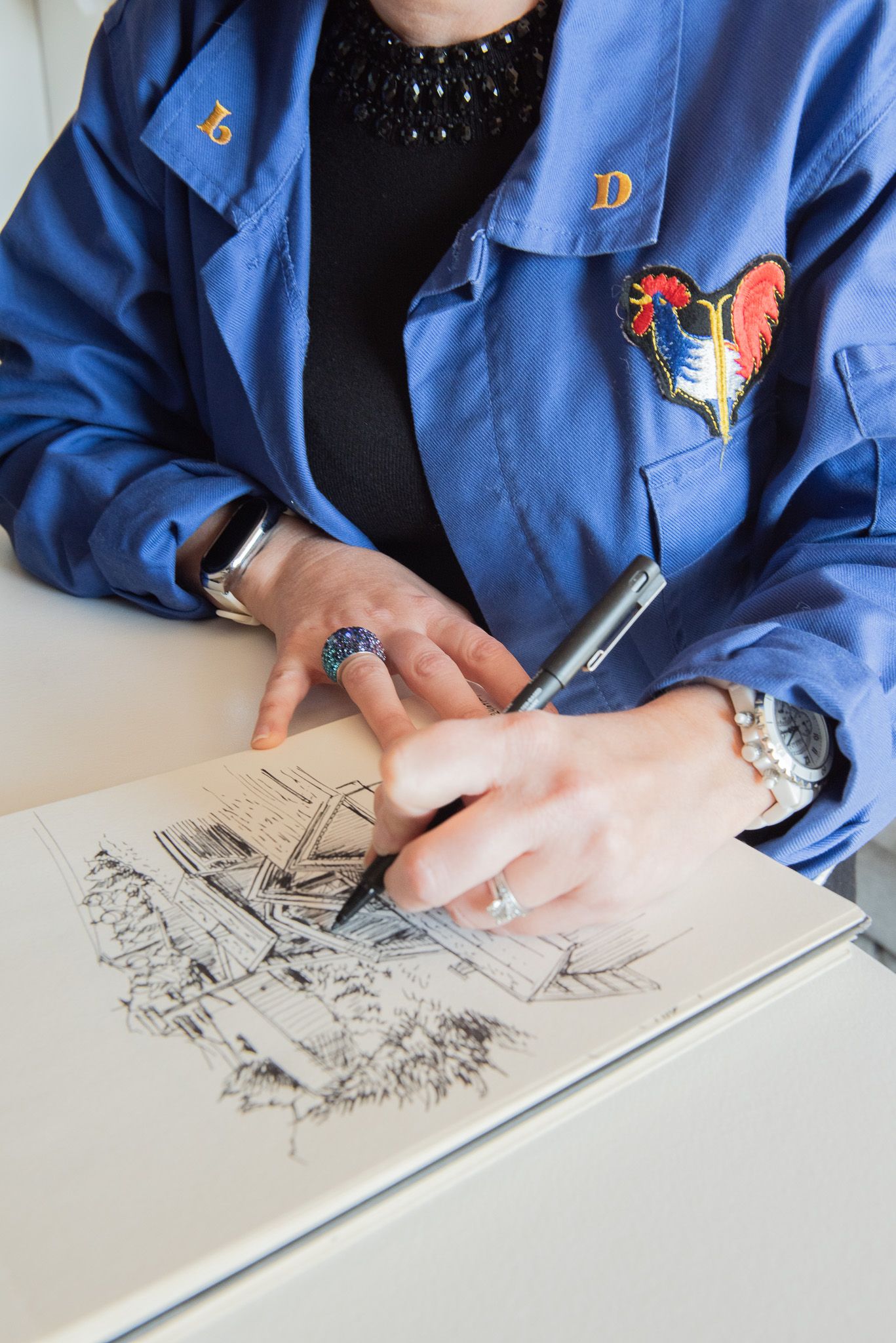 Femme en veste de travail personnalisée et brodée bleue réalisant un croquis architectural au stylo dans un carnet pour son shooting de bra.