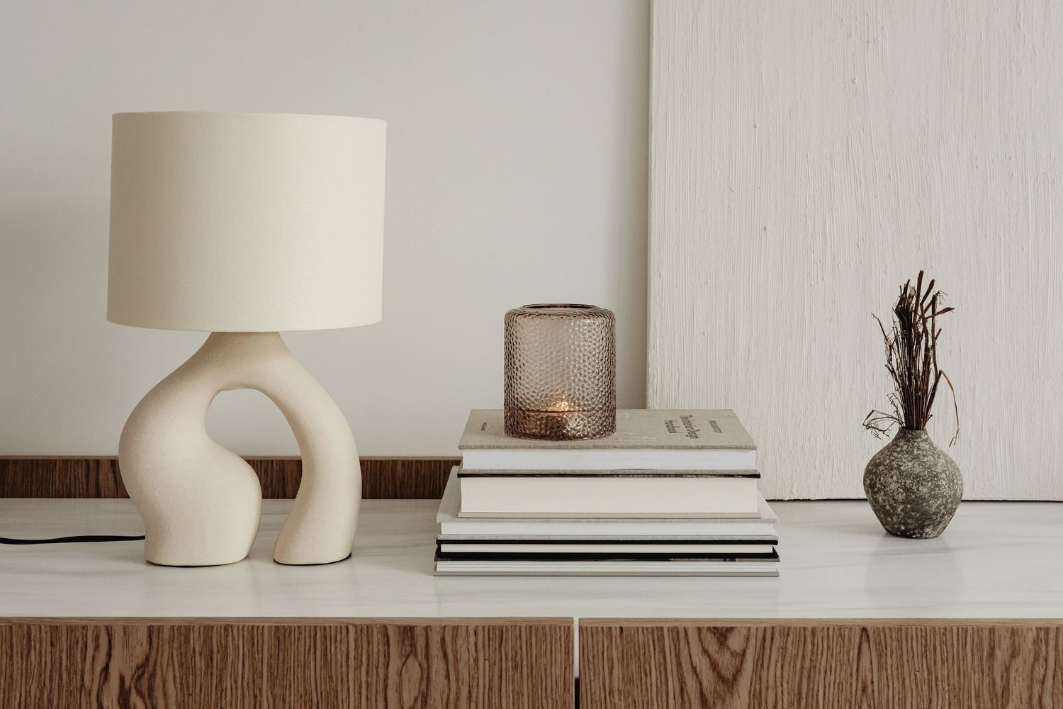 Décoration minimaliste d'étagère avec lampe en céramique, livres empilés, bougie et petit vase.
