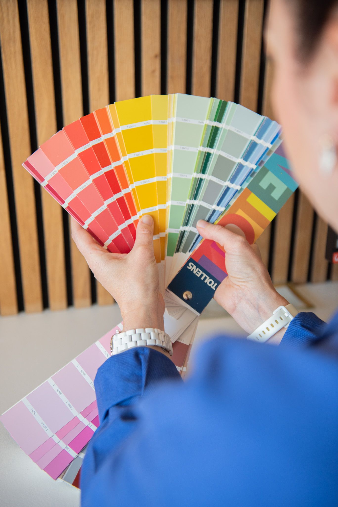 Une décoratrice d'intérieur tient des échantillons de peinture colorés de Tollens, étalés en éventail, présentant un large éventail d'option