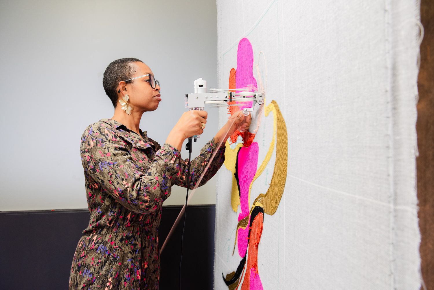 Artist using a heat gun to attach colorful pink and gold fabric pieces to a white canvas wall.