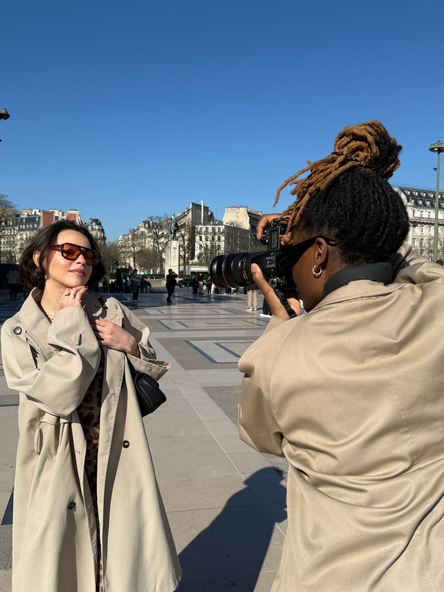 Photographe aux cheveux avec dreadlocks prenant le portrait d'une femme en trench-coat au Trocadéro à Paris lors d'un shooting de branging.