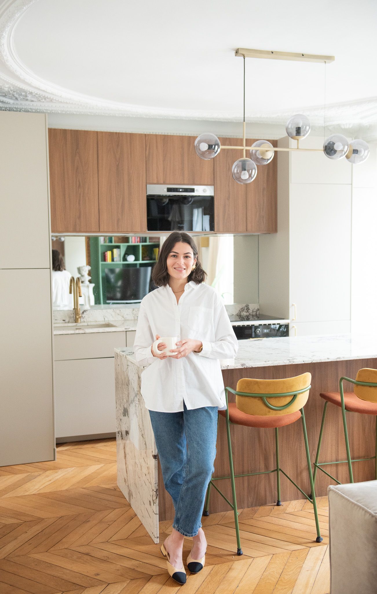 Smiling woman in white shirt leaning on marble kitchen island in modern Parisian kitchen.