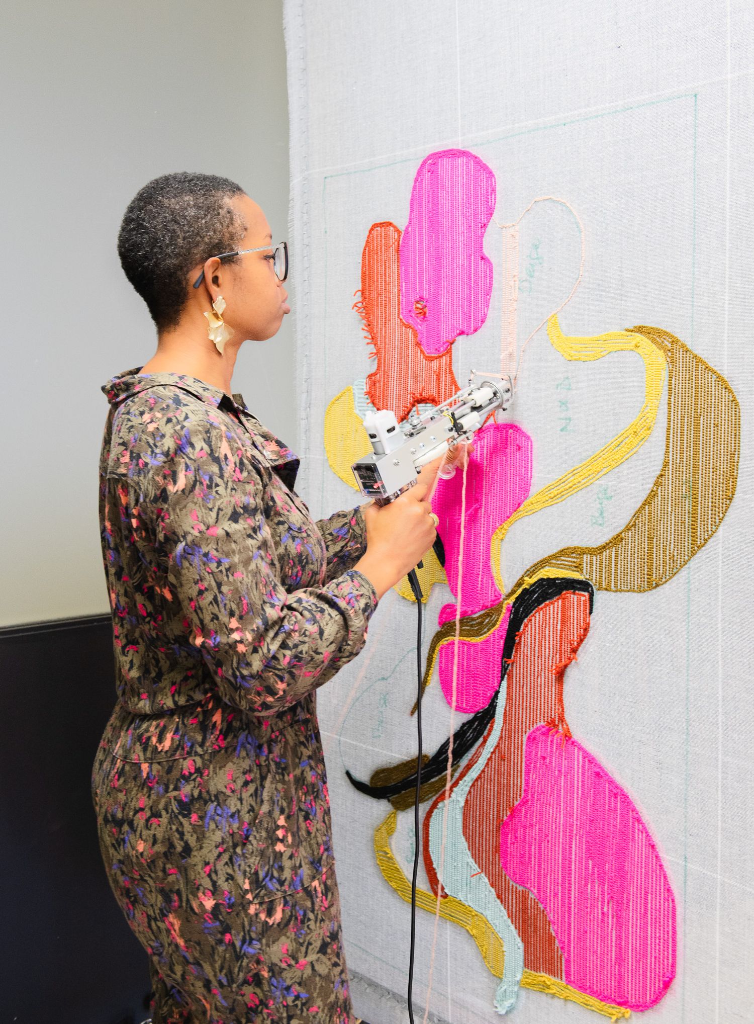 Textile artist uses electric tufting gun to create abstract pink and yellow fiber art wall piece.