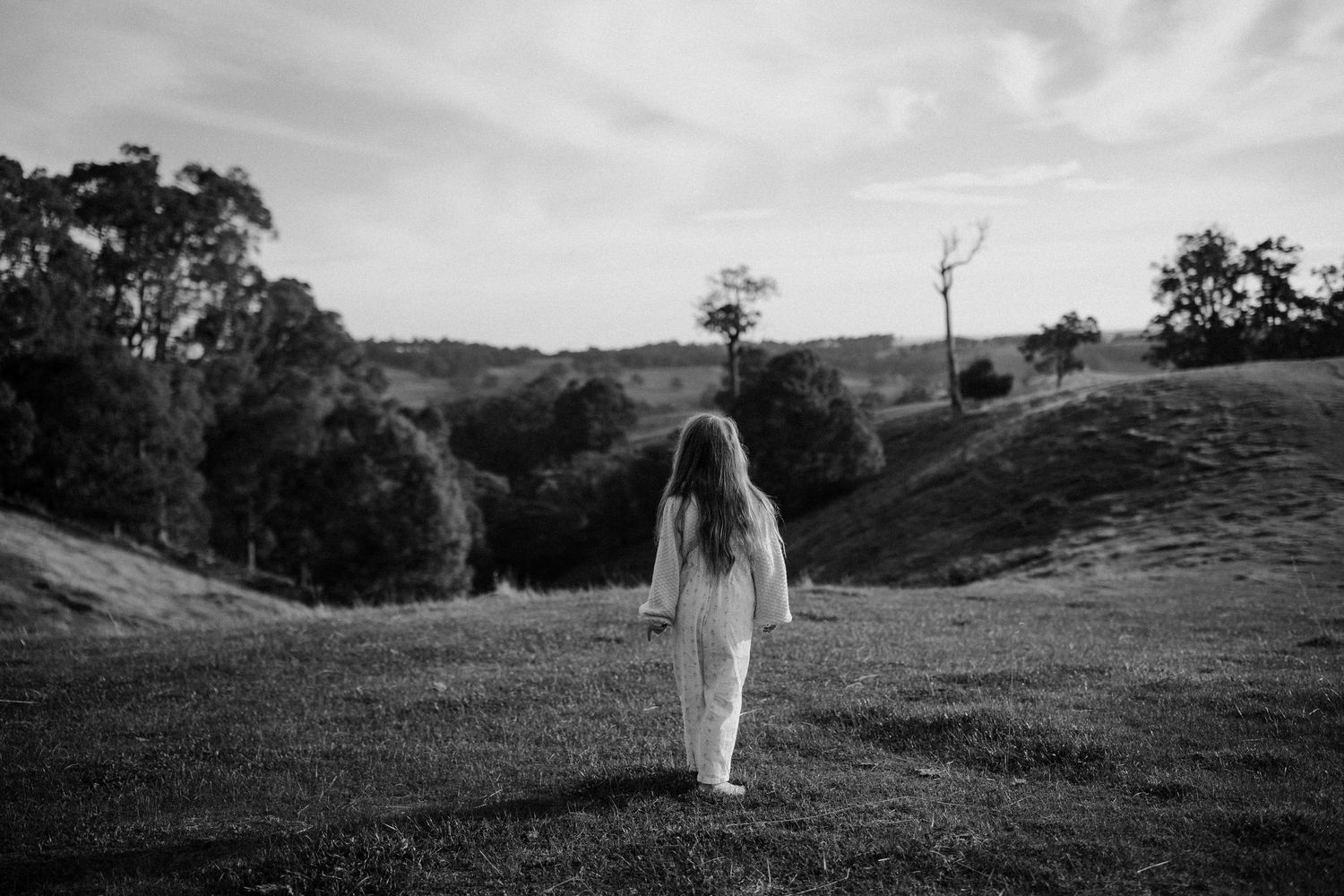 Black and white photo of a girl in white overalls walking through lush green rolling hills landscape in Ferguson Valley, Western Australia.
