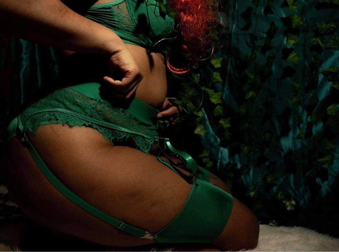 Boudoir by Hinton Imagery in Jacksonville NC. Close up of them in a green lingerie set pulling at the sides, you can see a leaf wall in back