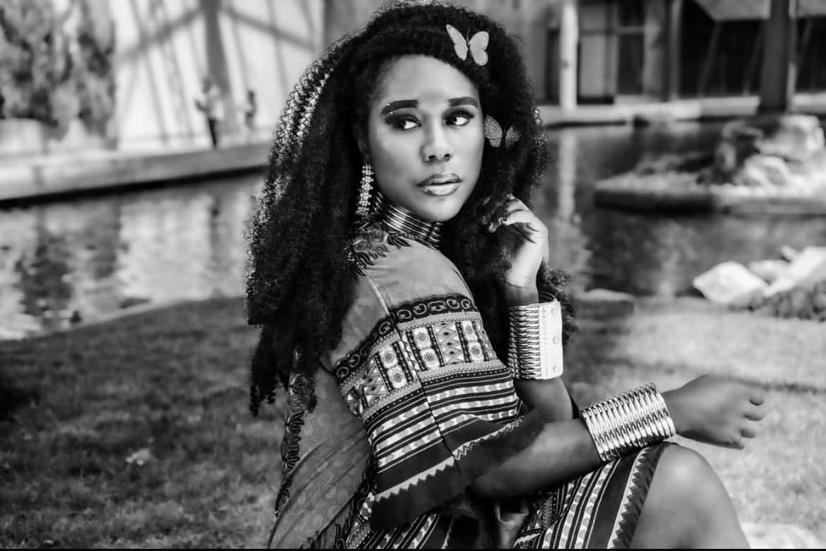 Stunning Black and White Image of a Black woman with butterflies in her wig wearing African patterned outfit and jewelry.