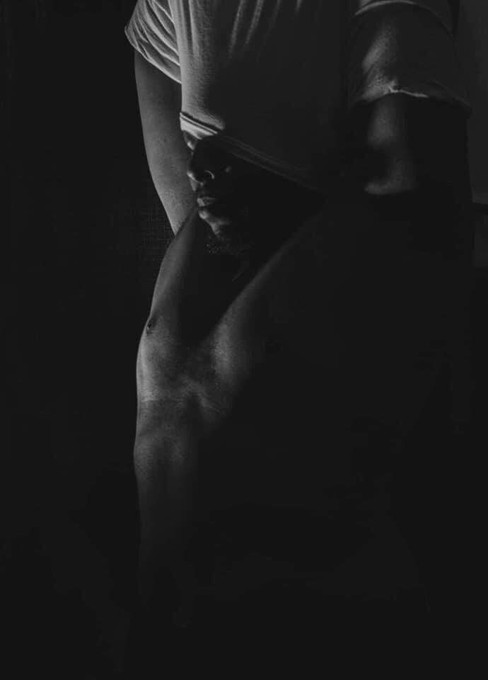 Black and white Image of a man pulling his t-shirt over his head. It is more of a silhouette, very dark and moody. Boudoir for men Hinton