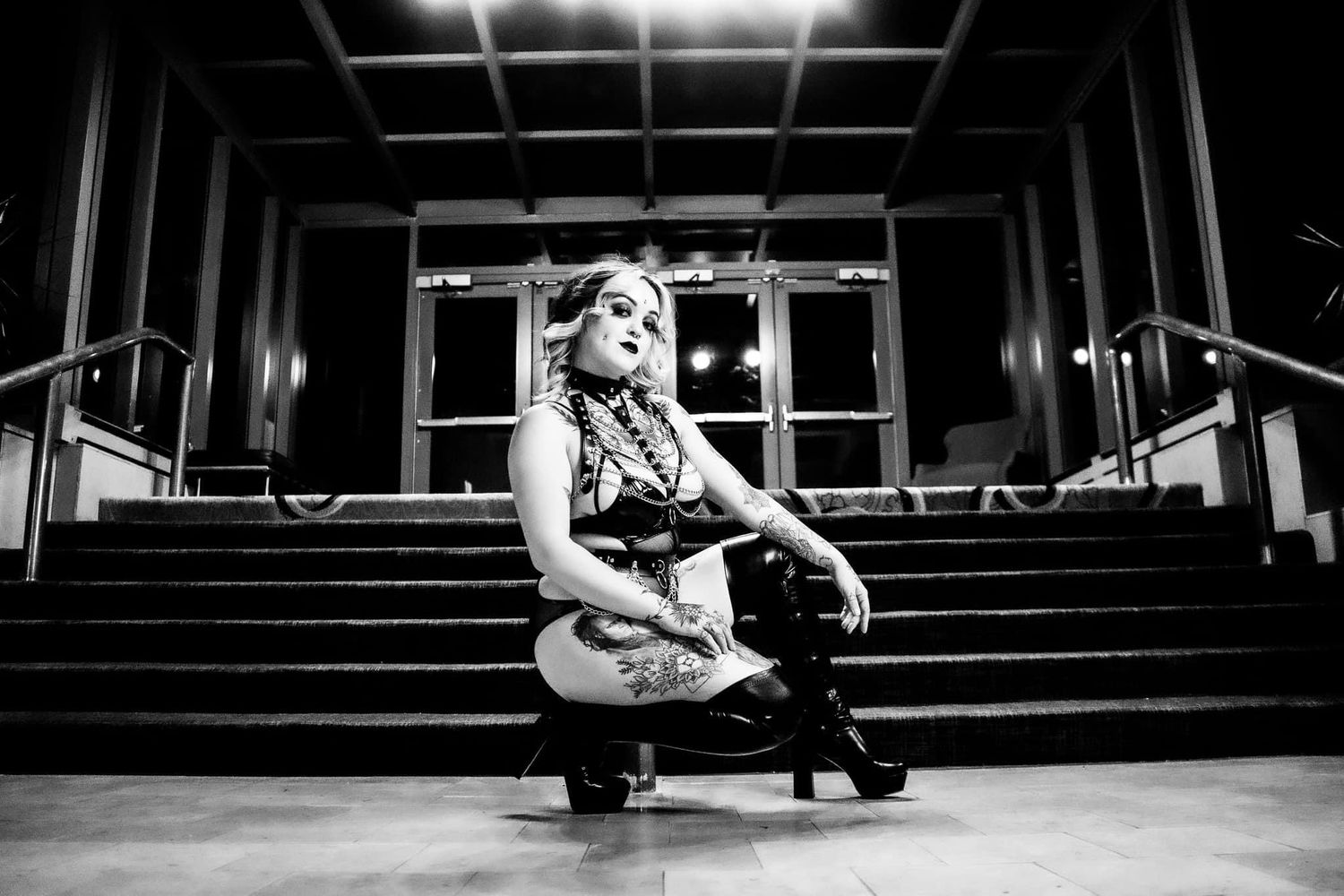 Black and White image of a Heavily tattooed White woman squatting down her thigh high boots. Boudoir by Hinton Imagery in Jacksonville NC