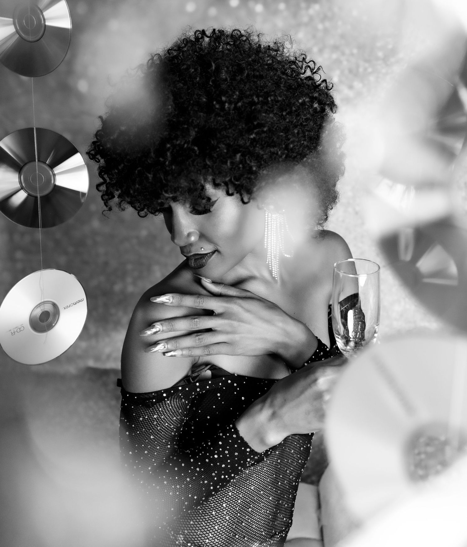 Black & white photo of Boudoir portrait in Jacksonville NC. Black woman with an Afro holding her shoulder and a glass in a sparkly bodysuit