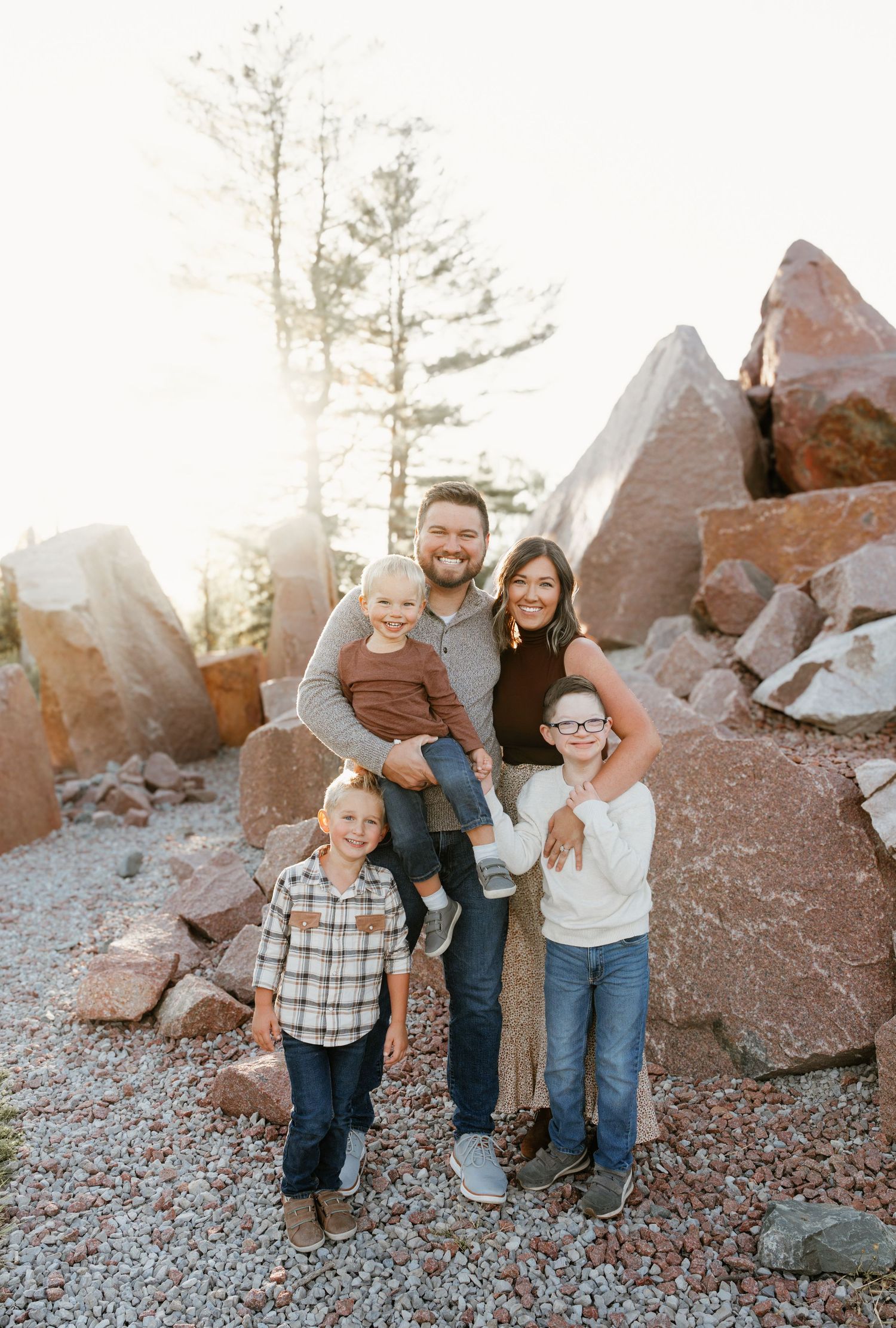 Family of five posing together among large red rocks and pine trees in a warm outdoor photo session.