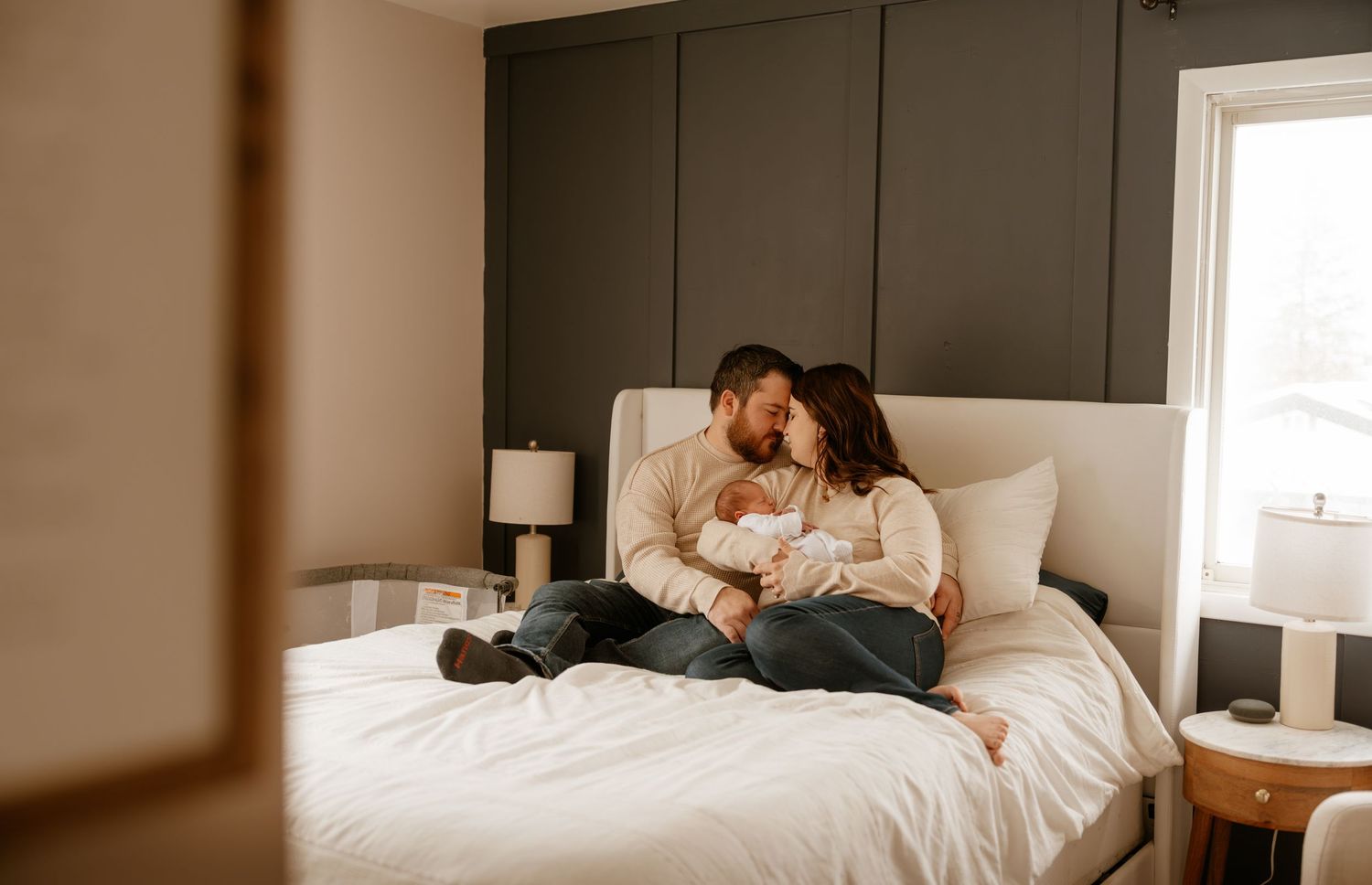 Couple snuggling with newborn baby on white bed.