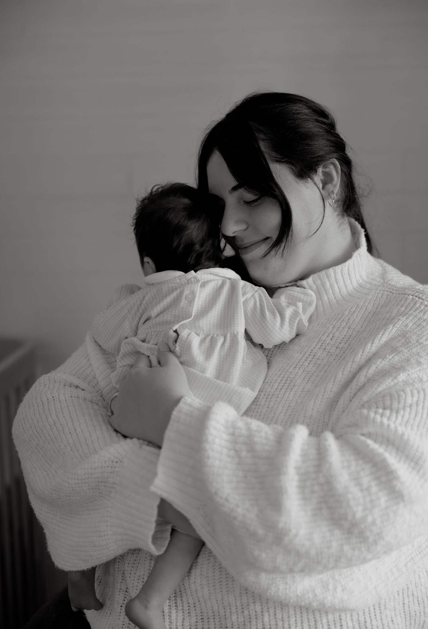 Black and white photo of a smiling mother tenderly holding her newborn baby close to her chest.