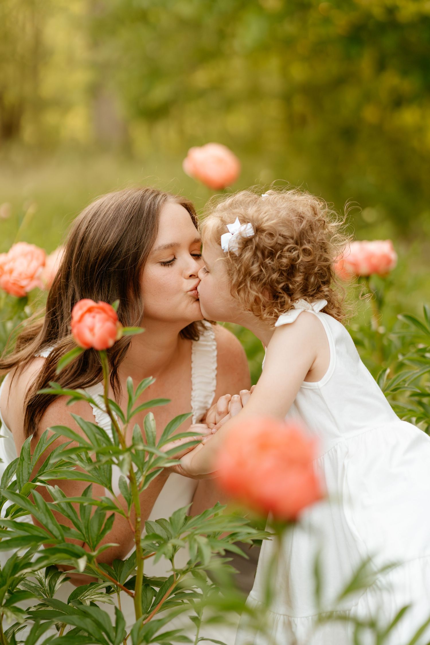 Intimate mother and child portrait series among blooming coral peonies in garden setting.