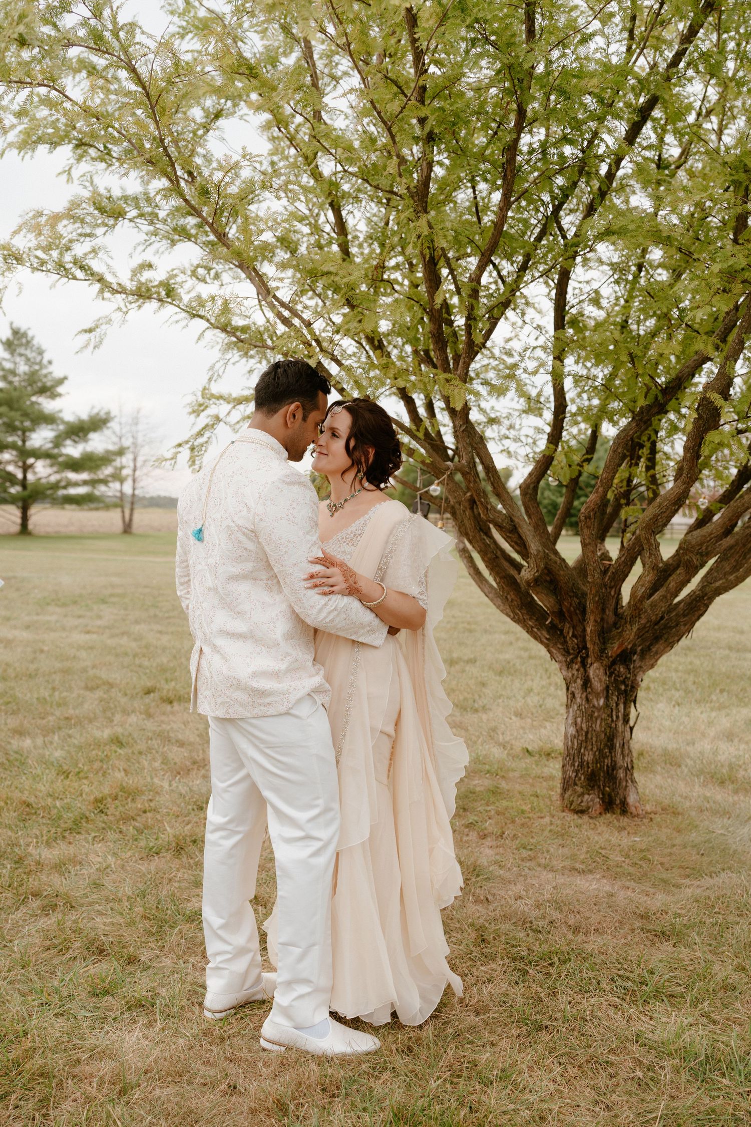 Romantic couple in white attire embracing under blooming tree.