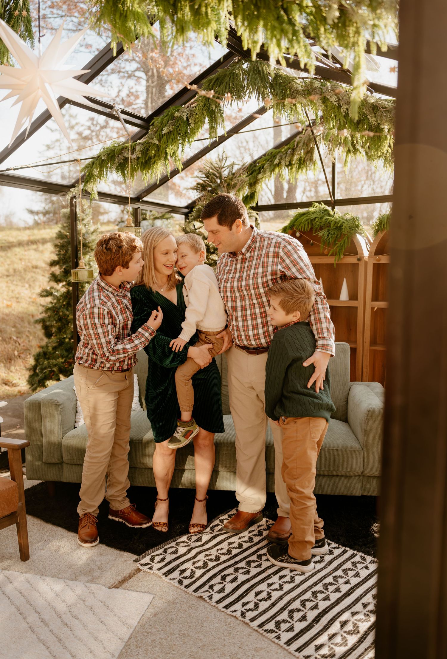 Family of five sharing a joyful moment in a festive greenhouse decorated with pine garlands during the holiday season.