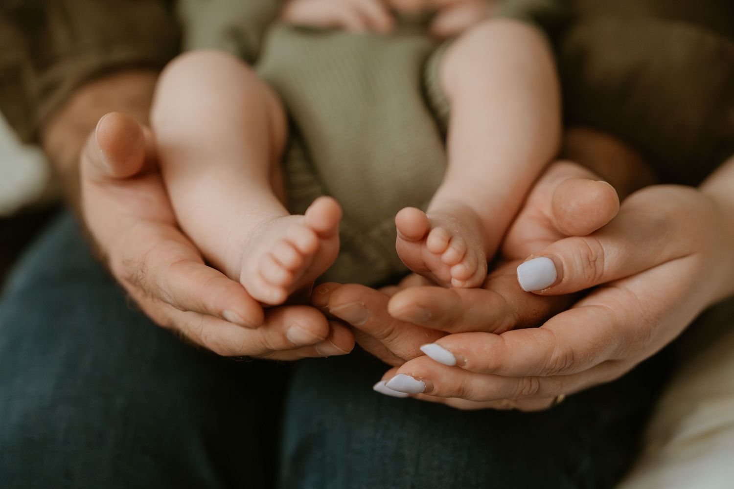 Two adult hands gently cradling tiny newborn baby feet, showcasing a tender family bonding moment.
