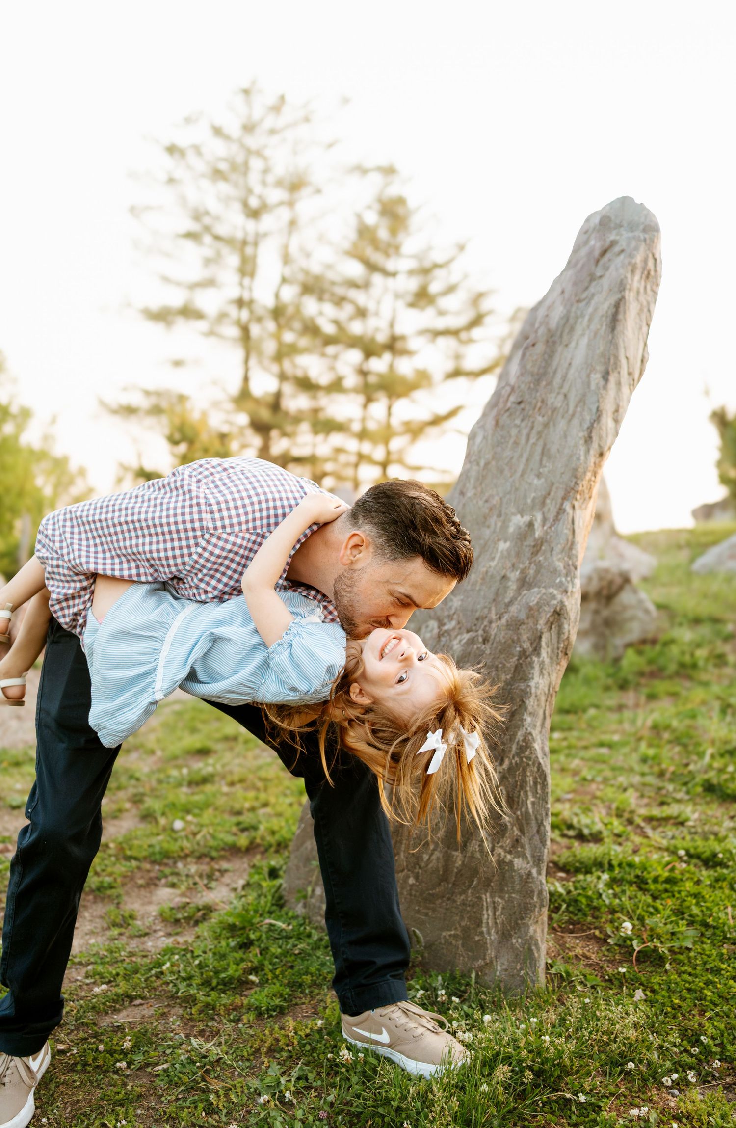 Couple shares romantic dip pose in grassy outdoor setting with trees.