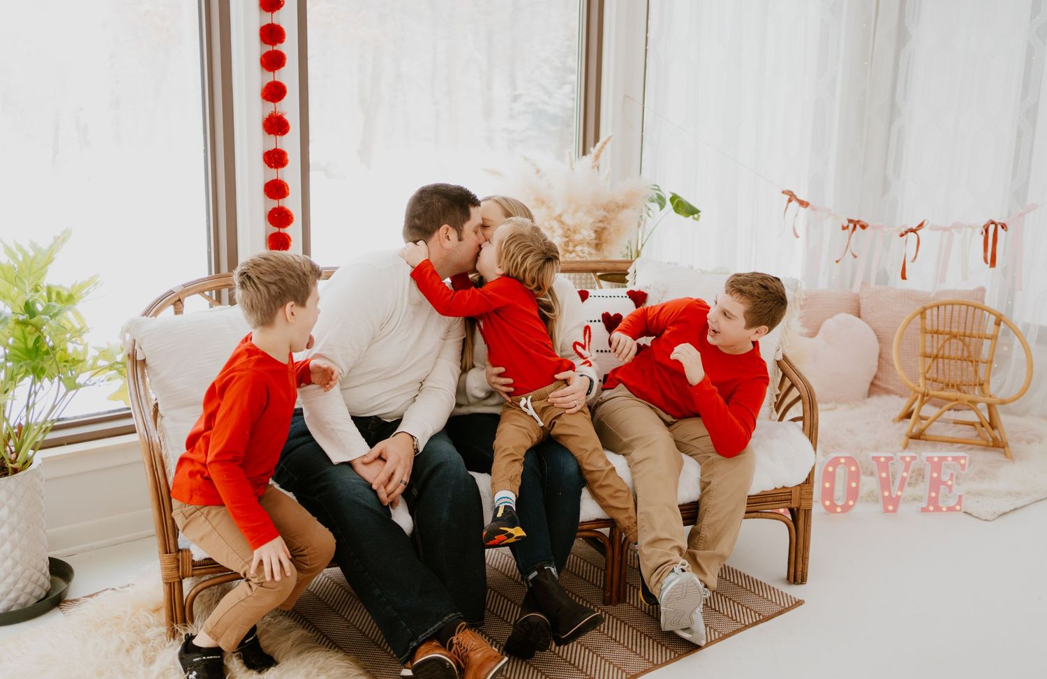 Family playfully interacting on chairs in a bright room with red and white holiday decorations.