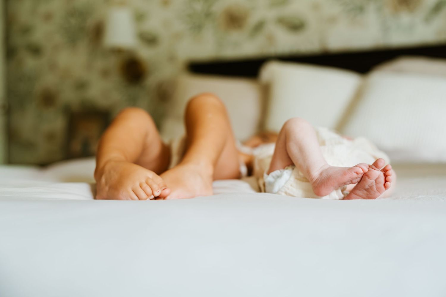 Adult and baby feet peeking out from white bed sheets, capturing a tender family moment in a cozy bedroom.