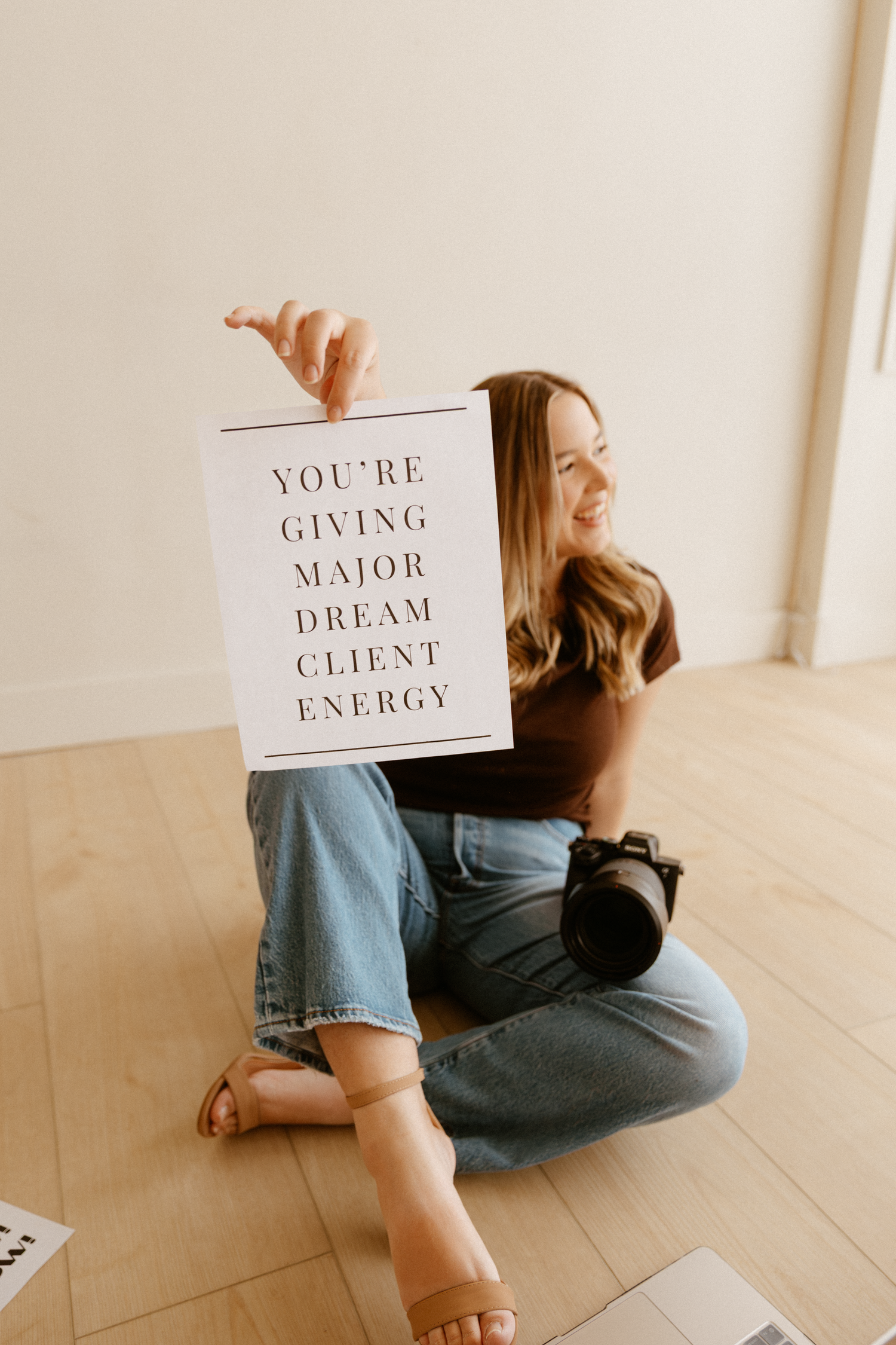 Photographer holding inspirational quote sign while sitting cross-legged on wooden floor.