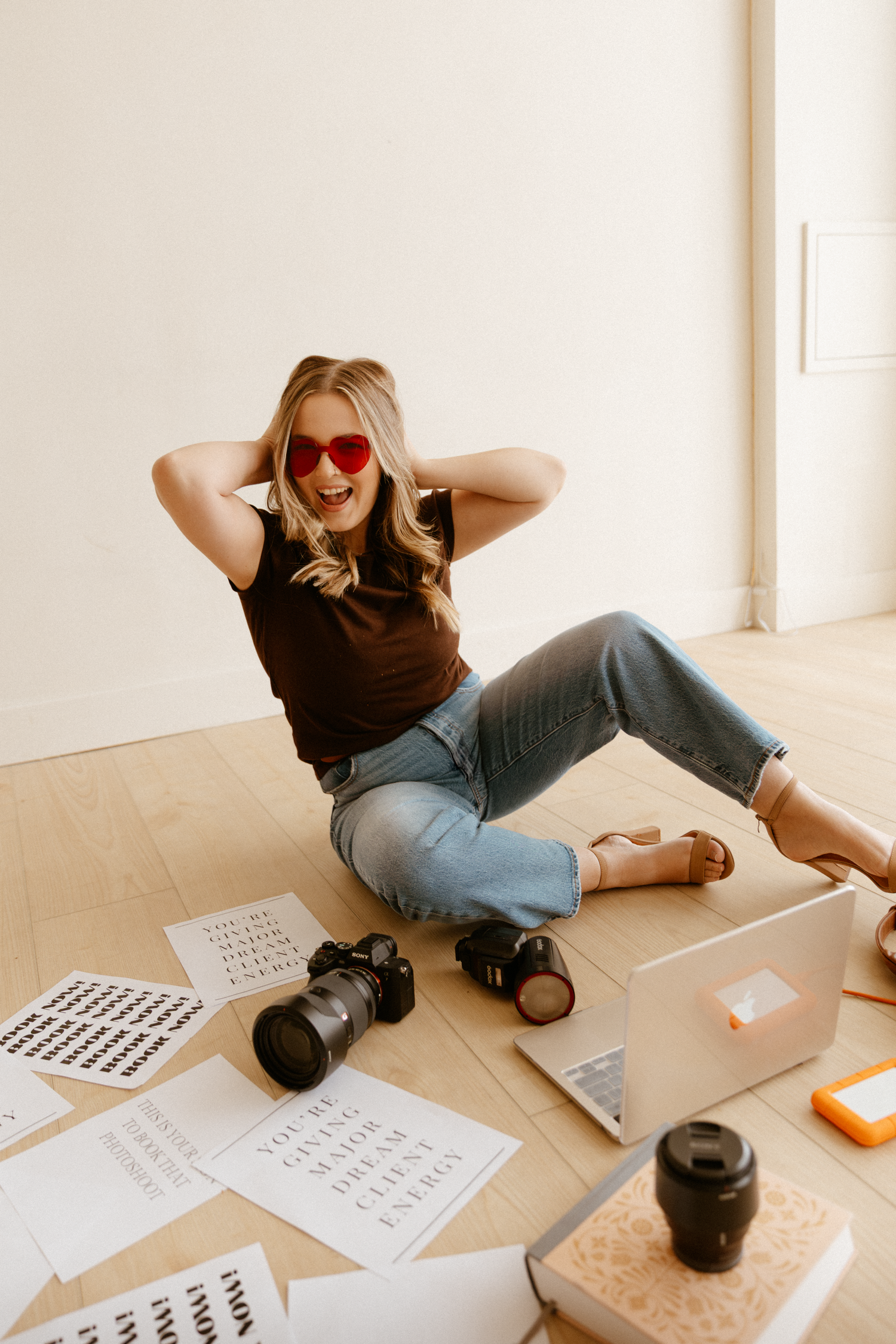 Person lying on wooden floor with heart-shaped sunglasses and laptop in casual setting.