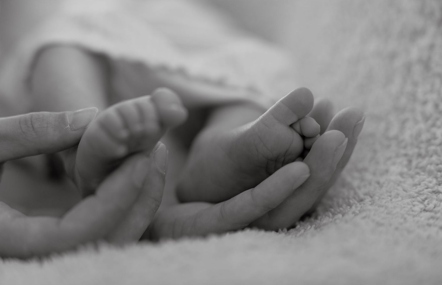 Black and white close-up of tiny feet resting on soft textured fabric.