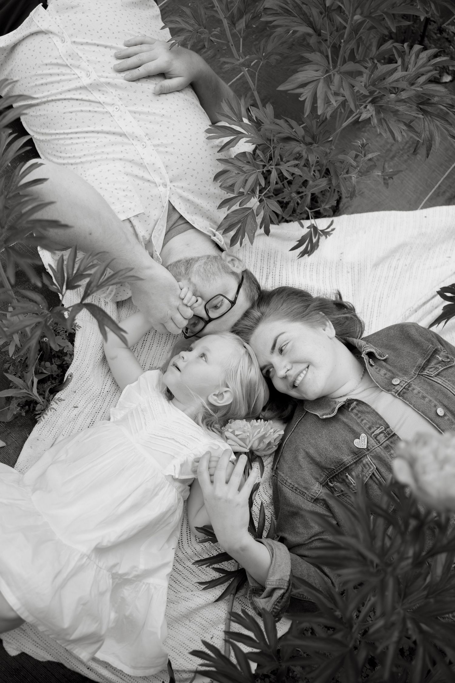 A black and white portrait of family members lying together among garden leaves.