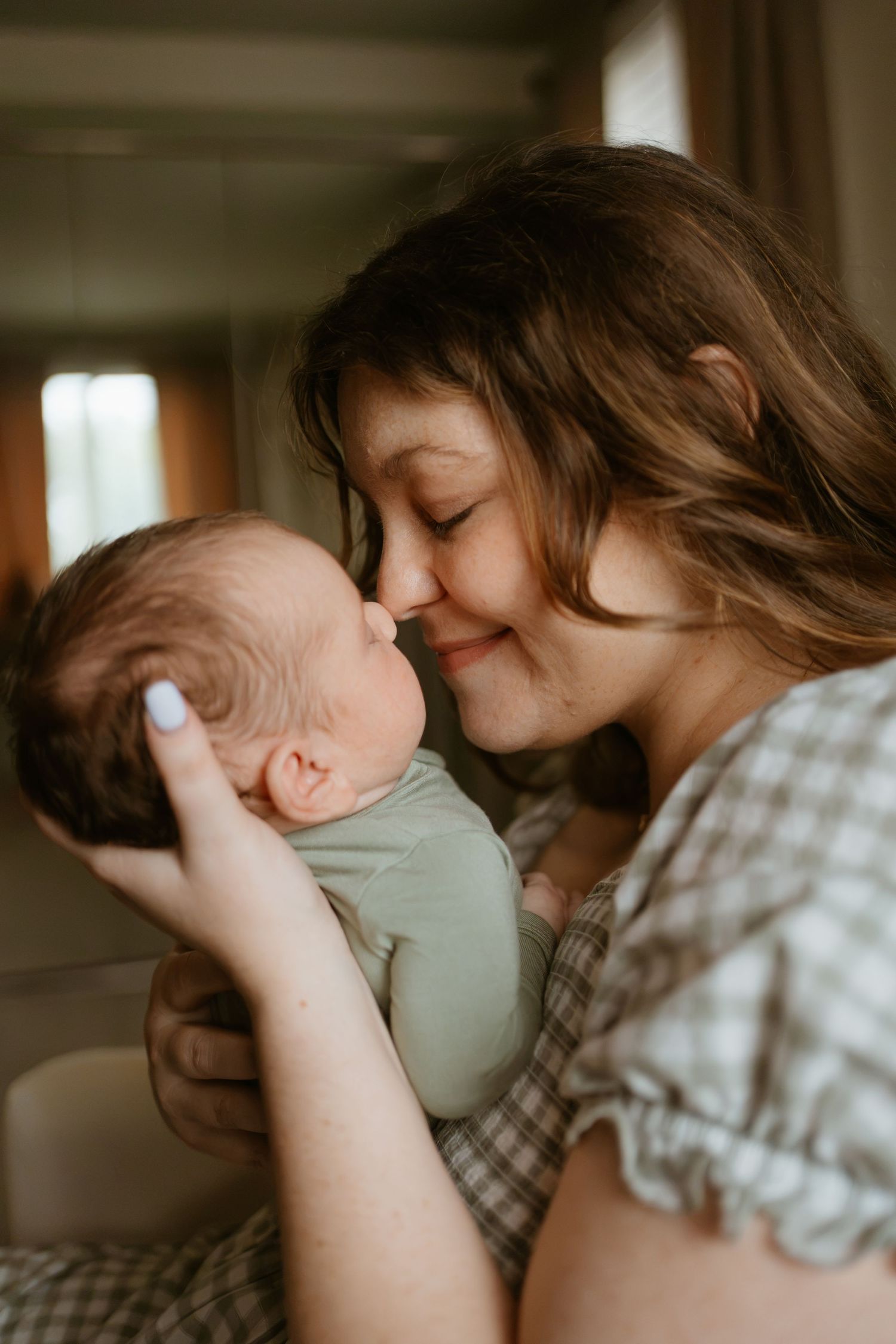 A mother tenderly nuzzles her newborn baby, cradling the infant in her hands with a warm, loving smile, located in Novi Michigan.