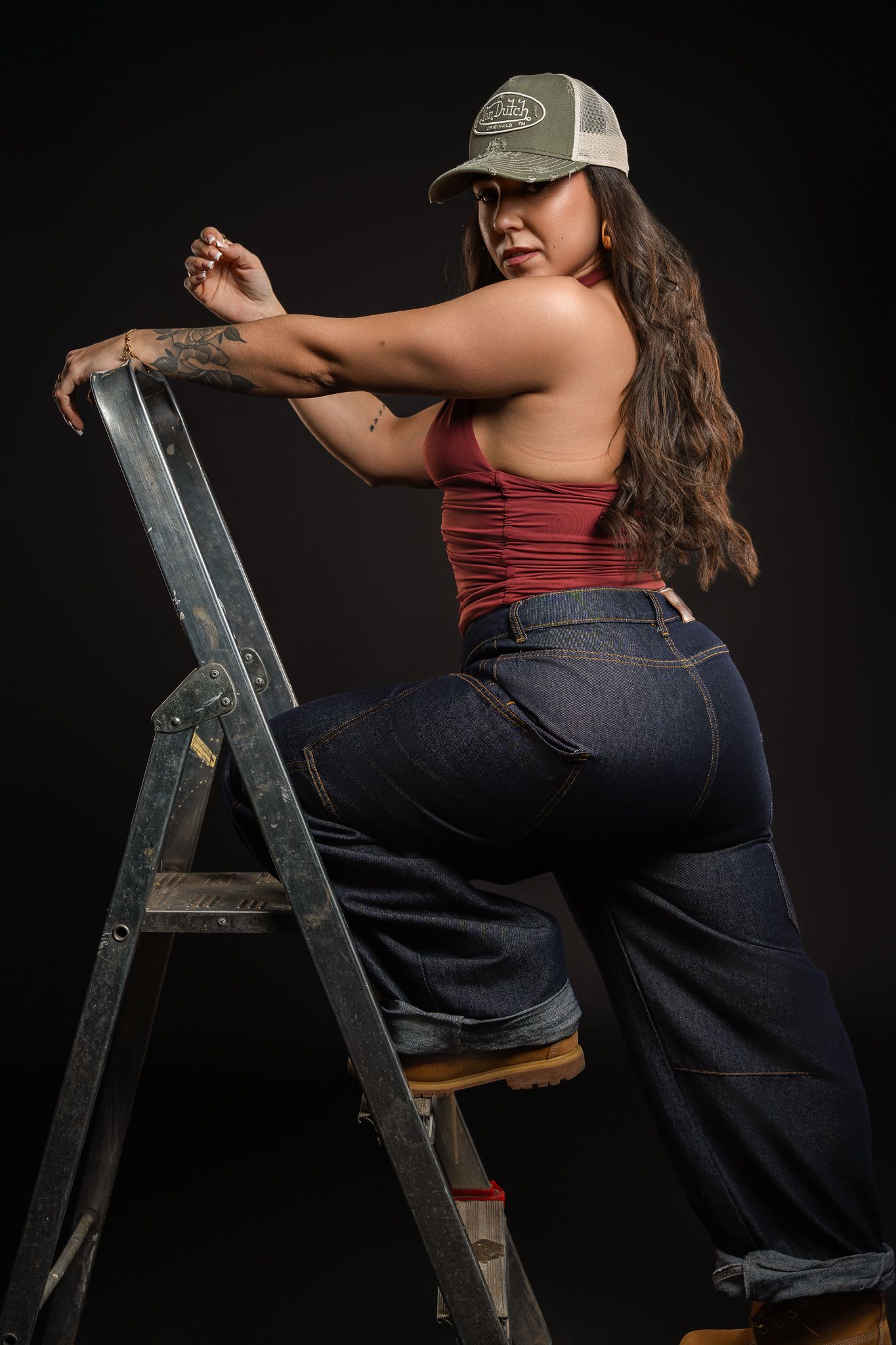 A person in jeans and a red tank top poses on a metal ladder against a black background in a series of shots.