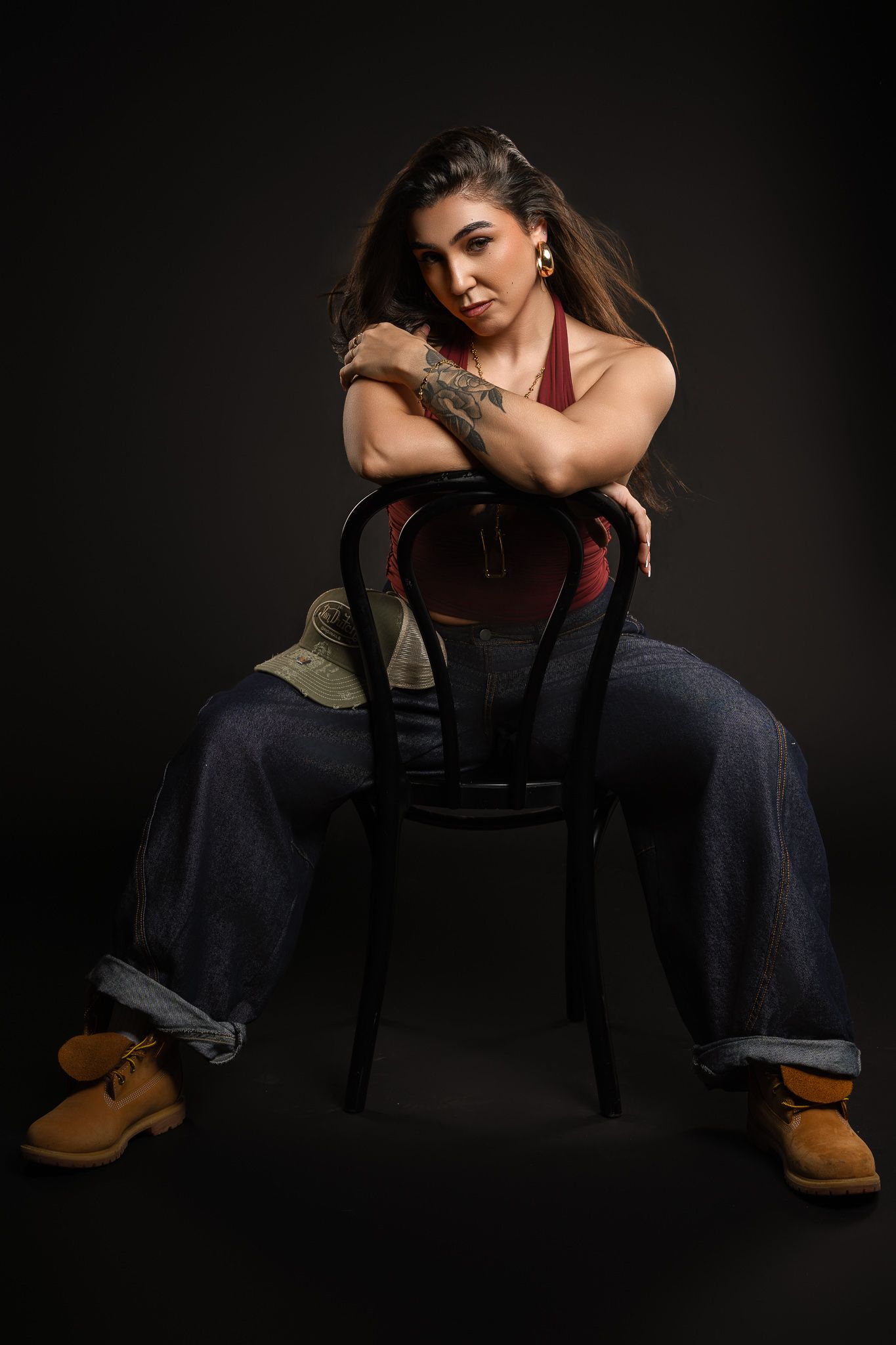Artistic portrait of dancer posing on chair in jeans and boots against dark backdrop.