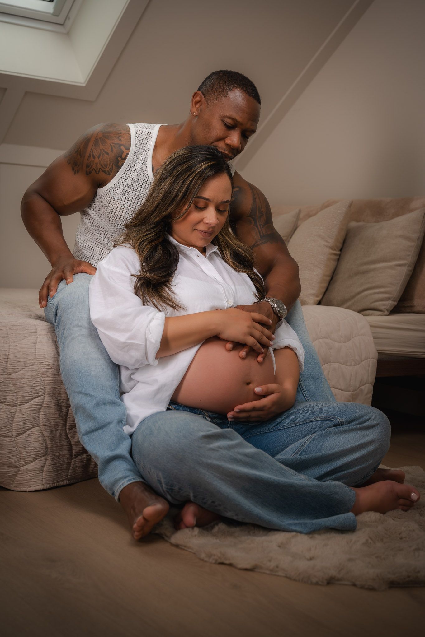 A pregnant woman and her partner share a tender moment on the floor, cradling her baby bump together.