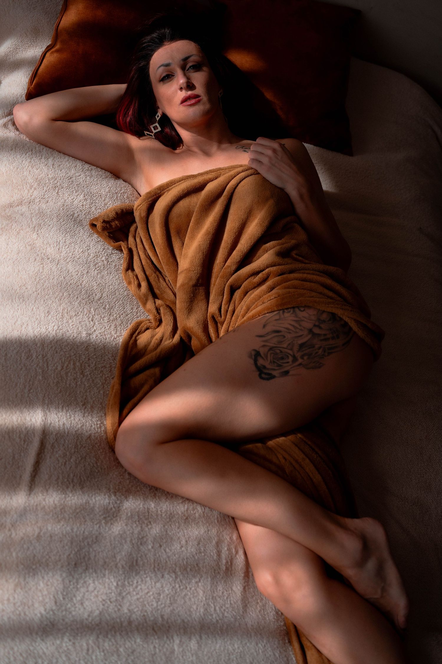 Boudoir portrait on white bedding with brown blanket and dramatic lighting.