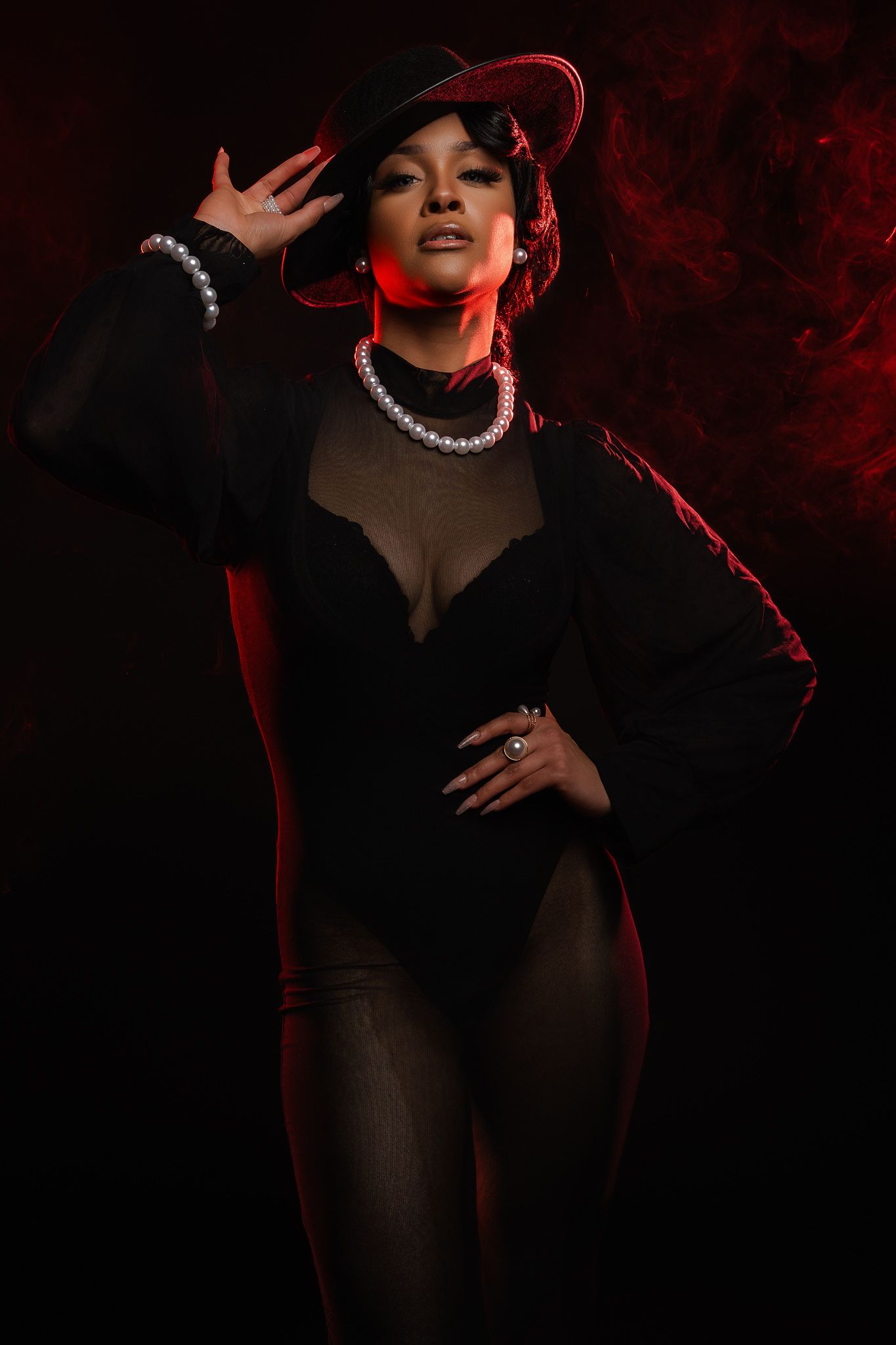 A dramatic fashion portrait series in red and black lighting shows a figure posing in dark clothing with pearl necklace.