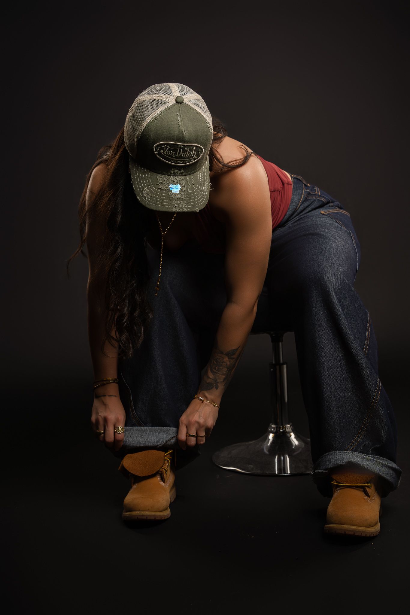 Person wearing dark jeans and brown work boots sits in a low position against black background.