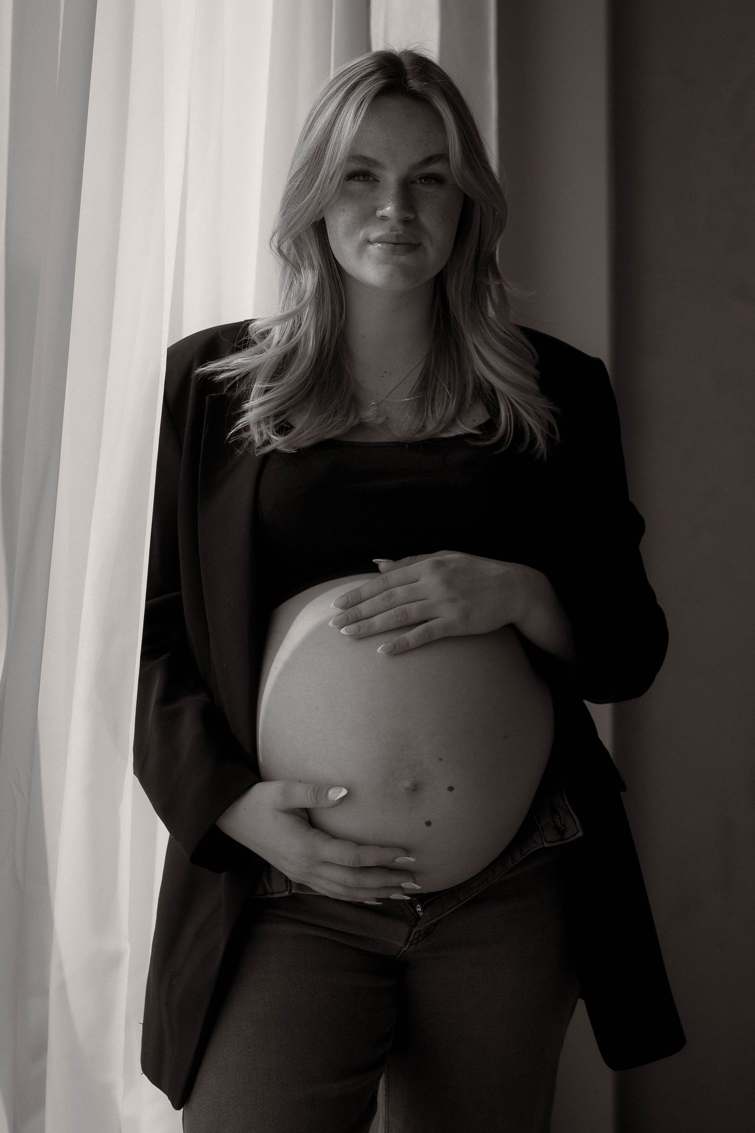 Black and white maternity photos showing a pregnant belly with gentle window lighting.
