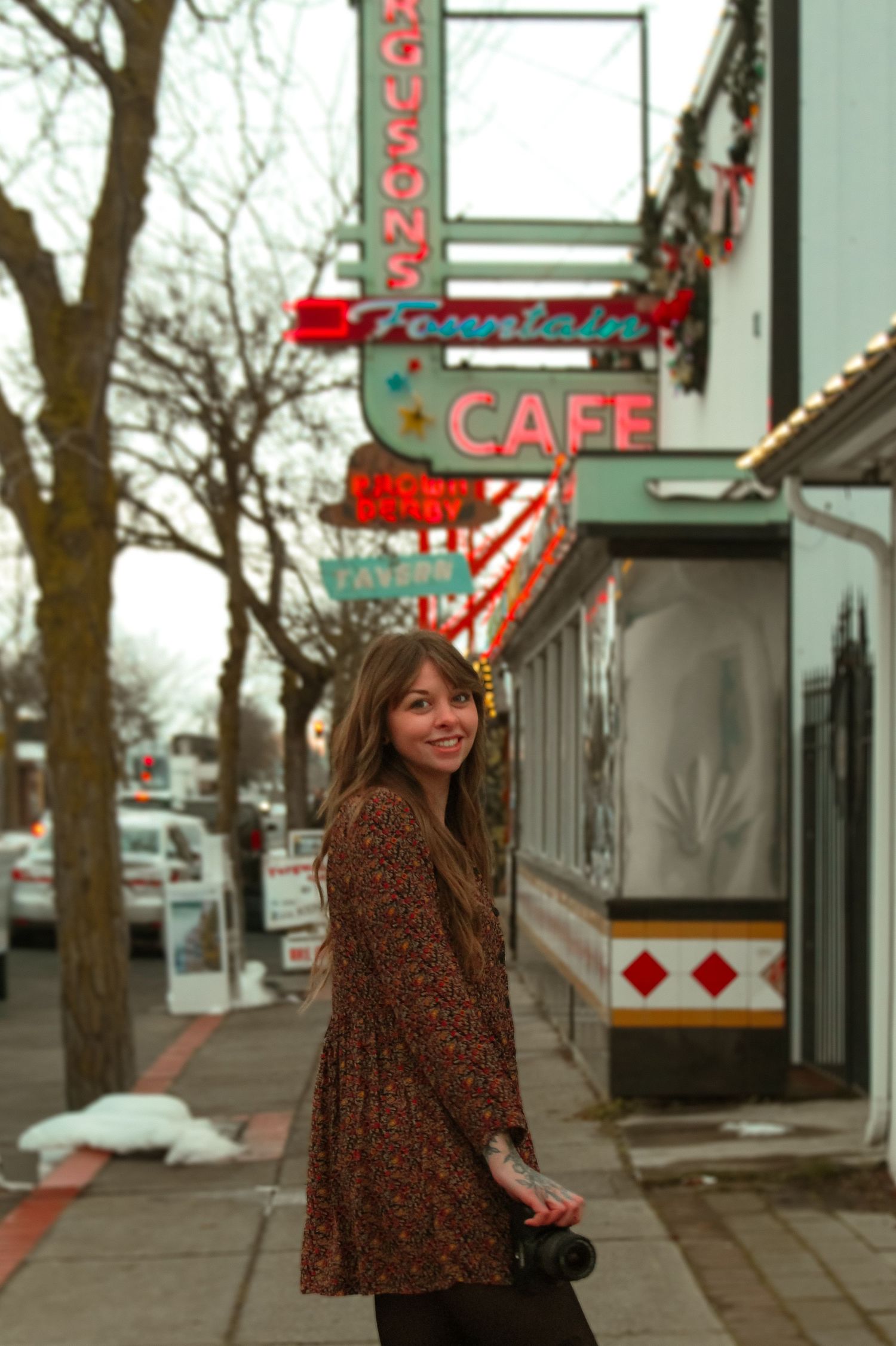 A woman in a floral dress smiling on a sidewalk near Ferguson's Fountain Cafe sign.