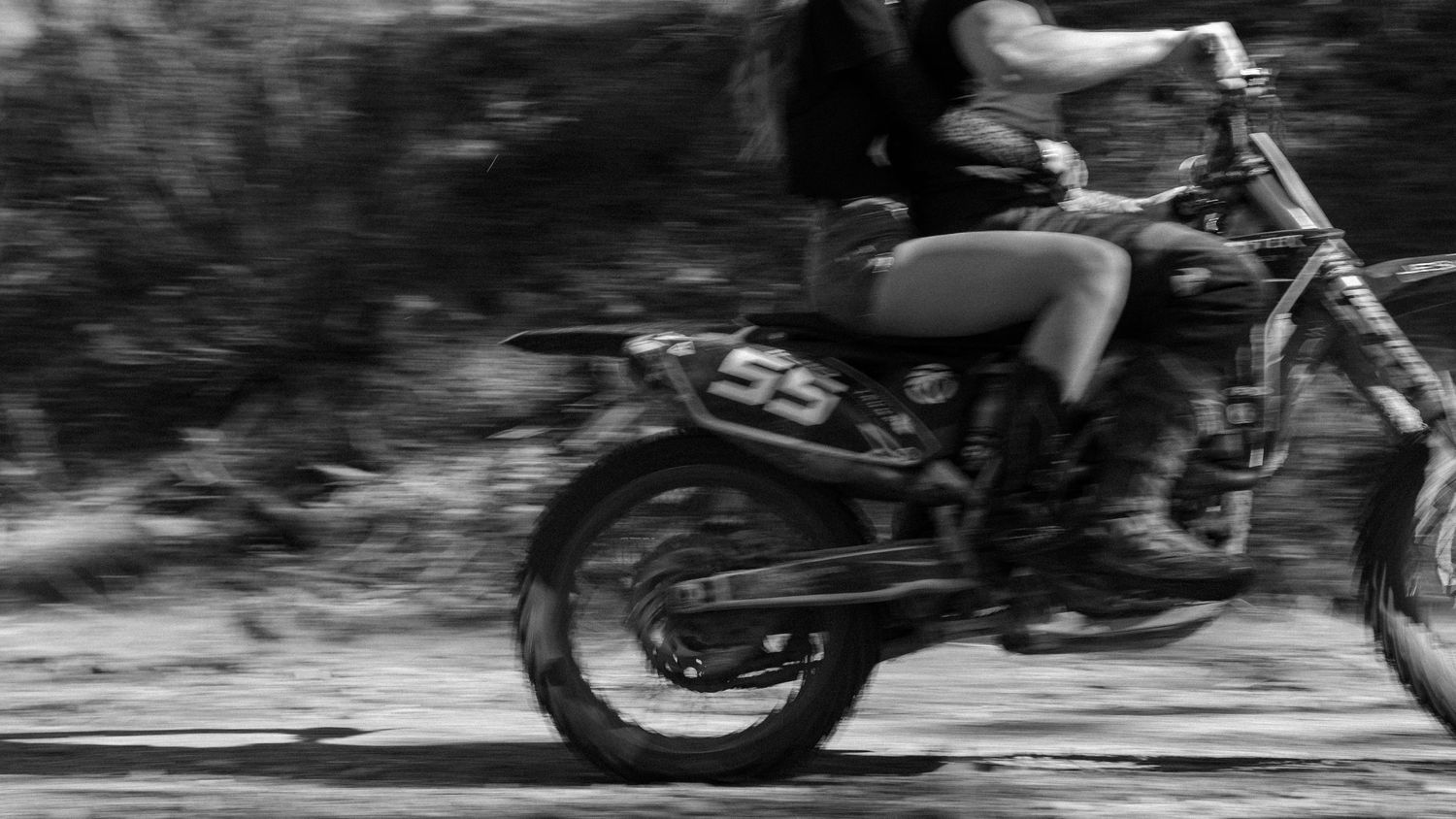 A rider on a dirt bike numbered 55 speeds down a road in a dynamic black and white action shot.