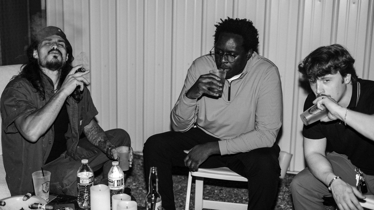 Three men sitting together in a black and white photo, relaxing and drinking in a casual indoor setting.