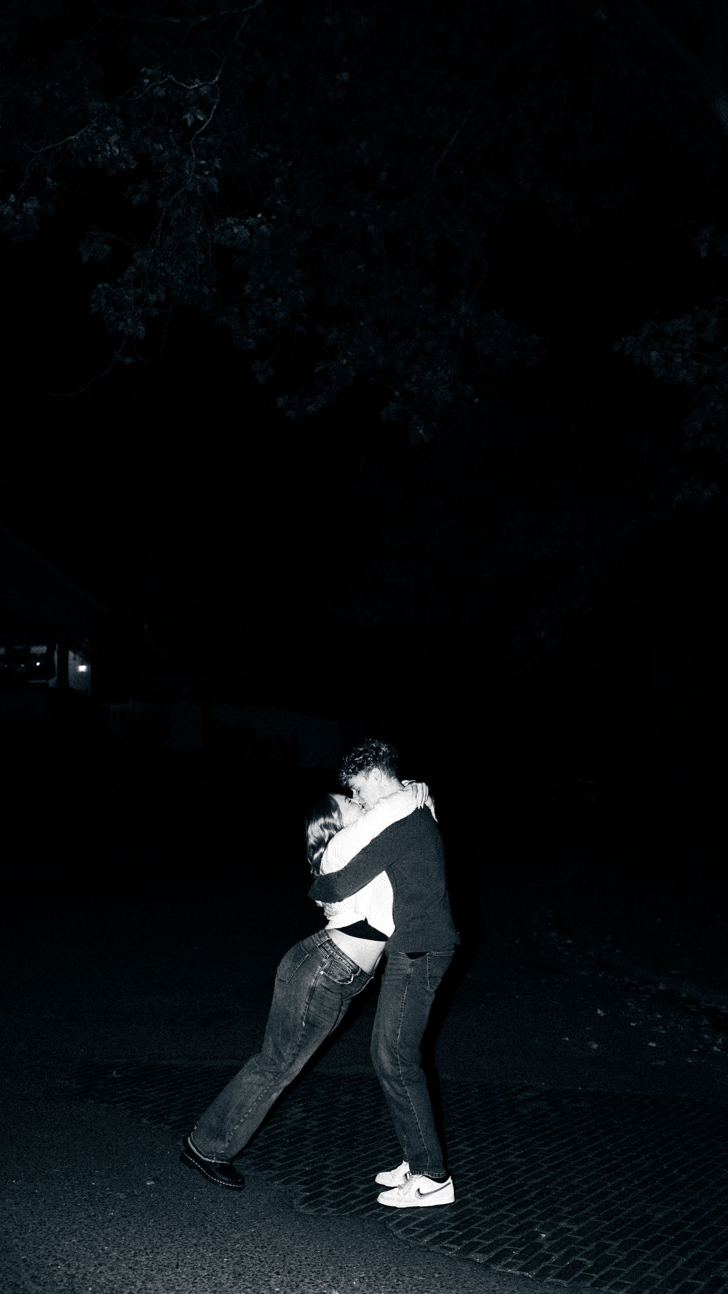 Couple embracing and dancing on a dark street at night in black and white photo.