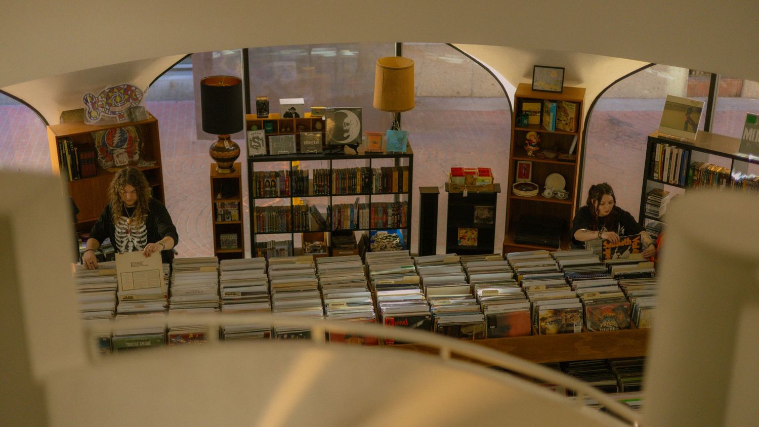 Two people browse a cozy bookstore filled with shelves of books and vinyl records.