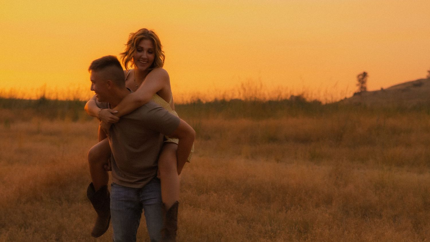 Couple sharing a romantic piggyback ride in a golden field at sunset.