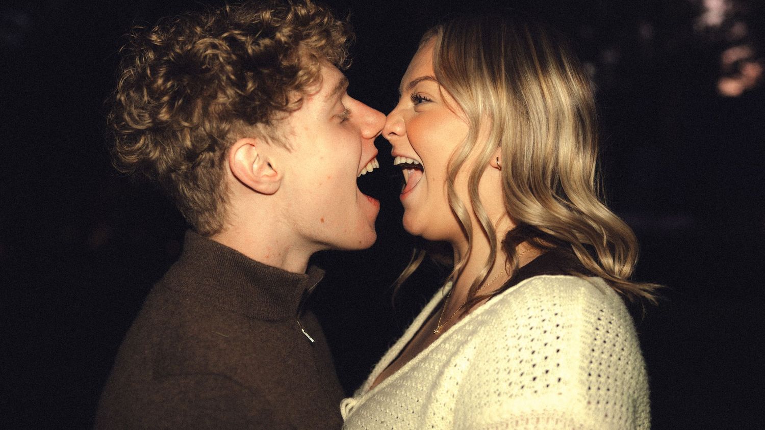 A joyful young couple laughing and sharing a romantic moment outdoors at night.