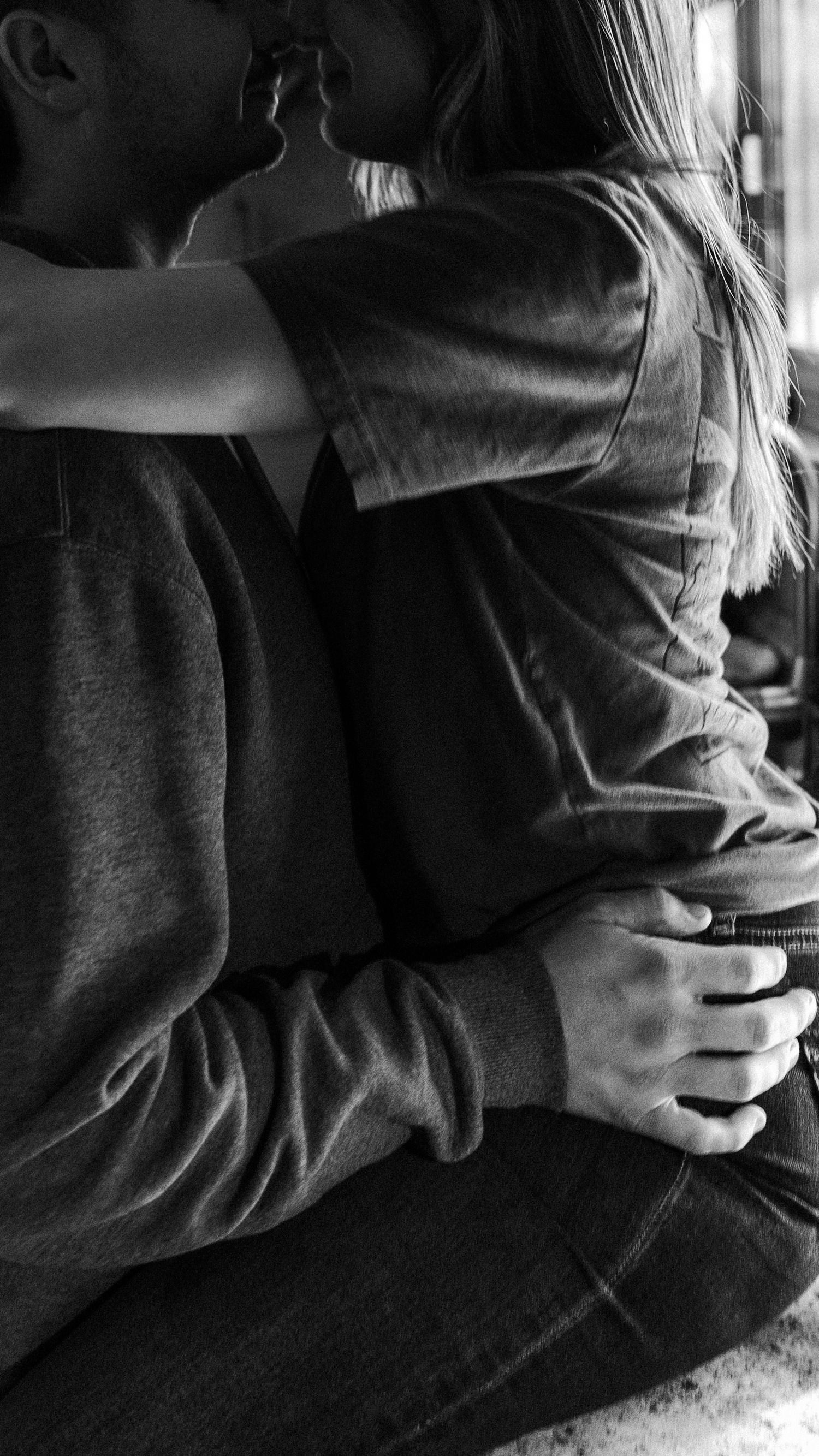 Black and white photo of a couple embracing and kissing, hands intertwined, wearing casual sweatshirts.