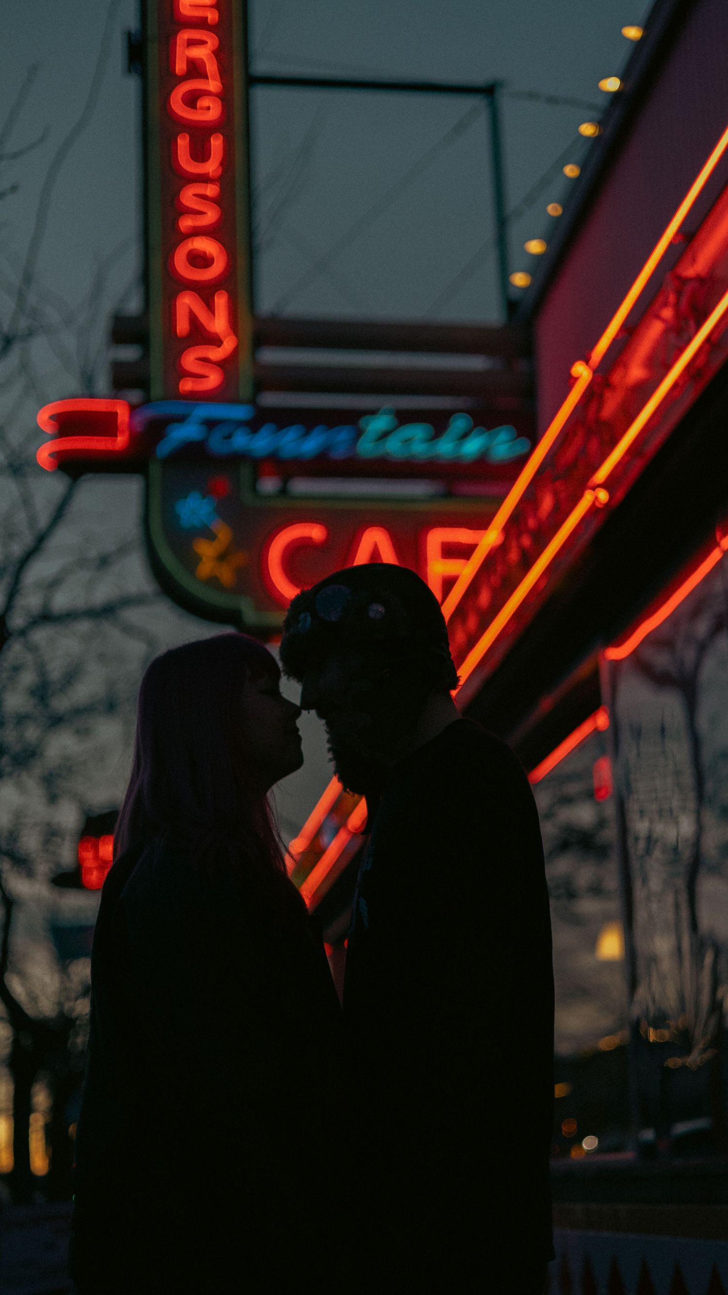 A couple silhouetted against glowing neon signs outside Ferguson's Fountain Cafe at dusk.