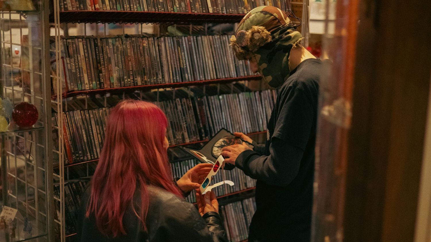 Two people browse vinyl records in a dimly lit music store, one with red hair and one wearing a colorful headwrap.