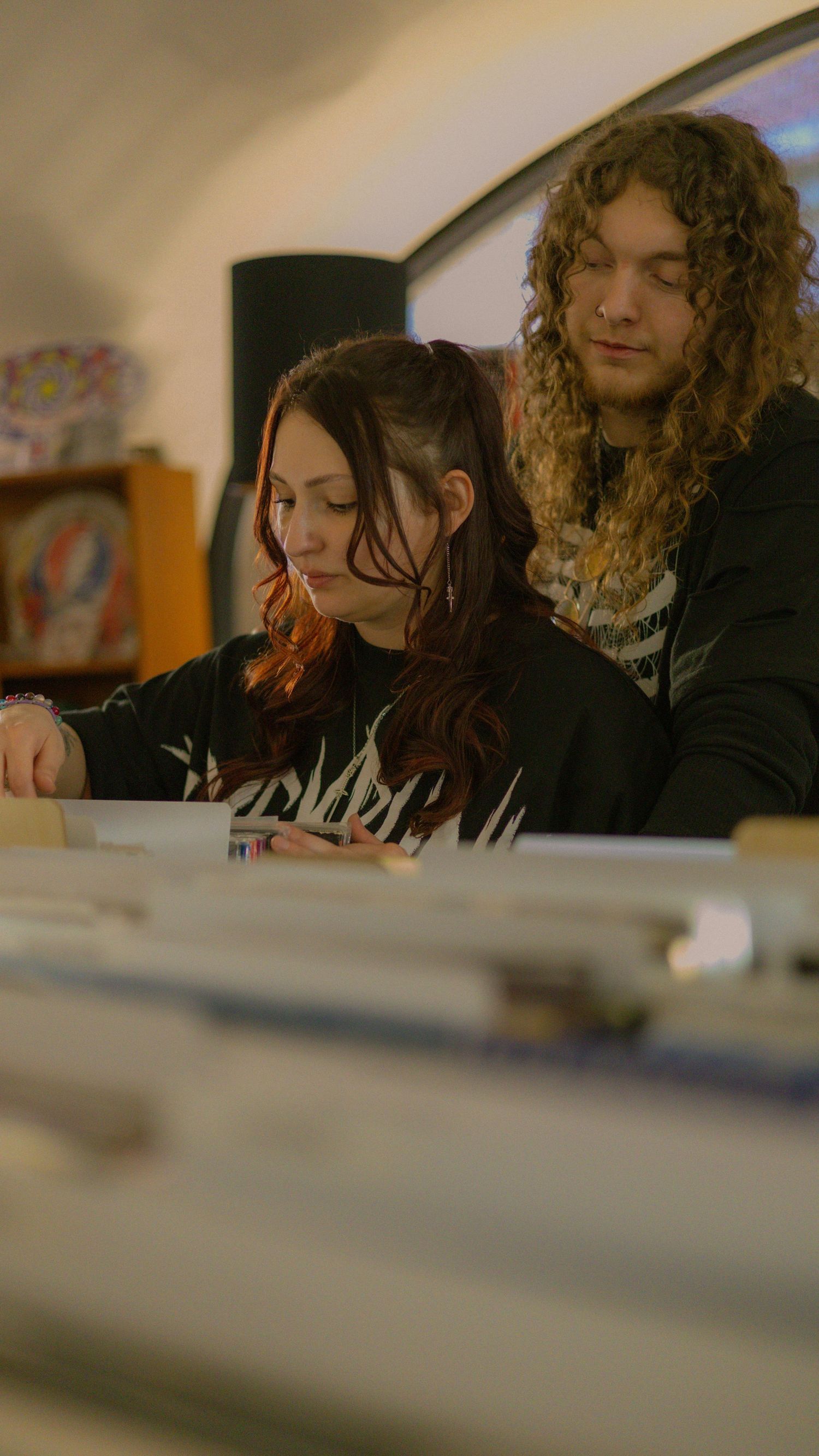 Two young adults with long hair browse vinyl records together in a music store.
