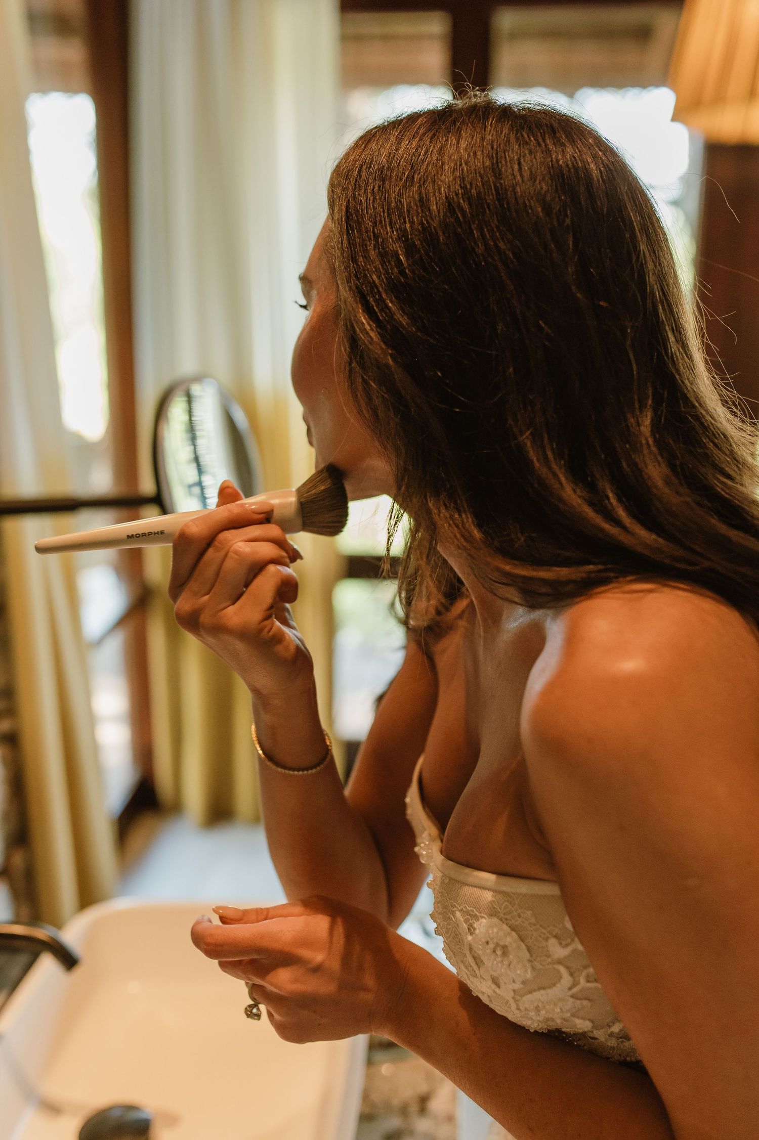 Bride applying blush makeup with a large brush while getting ready for her wedding day.