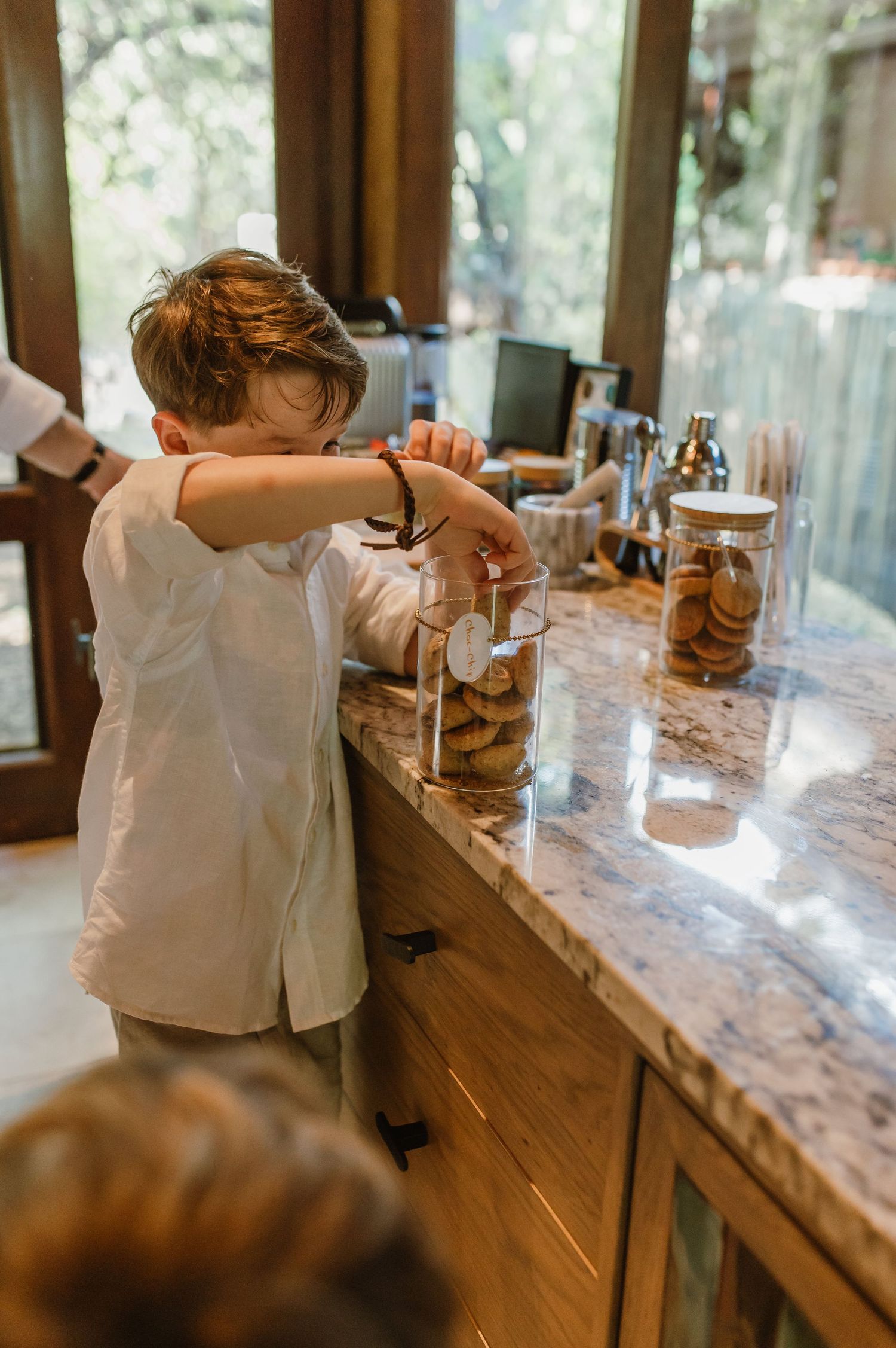 Young boy reaching into a cookie jar on a marble countertop in a luxury safari lodge kitchen.