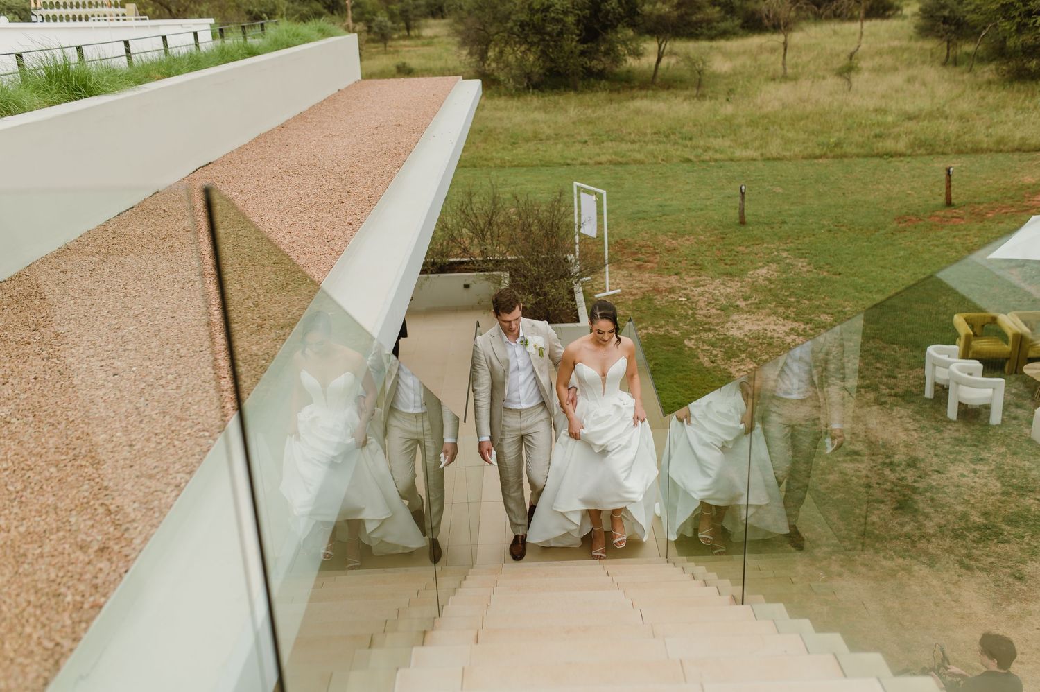 A wedding couple walks down a scenic outdoor path lined with trees and greenery on their special day.